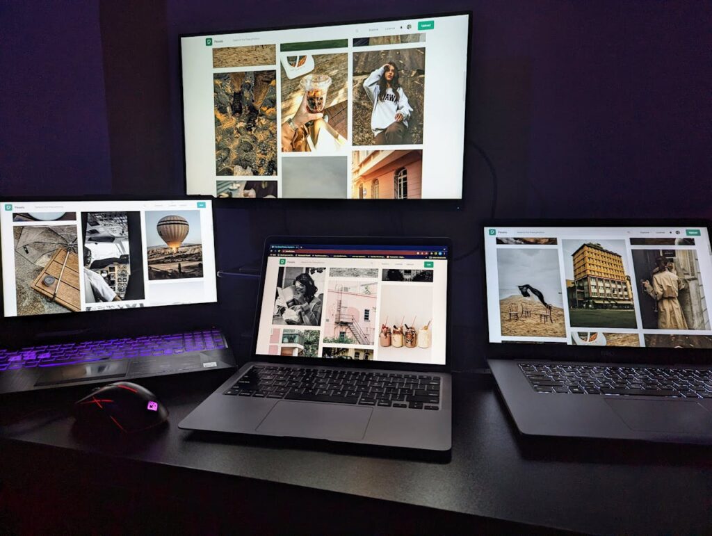 Three laptops and a monitor on a desk displaying creative graphic designs. Perfect for tech-focused projects.